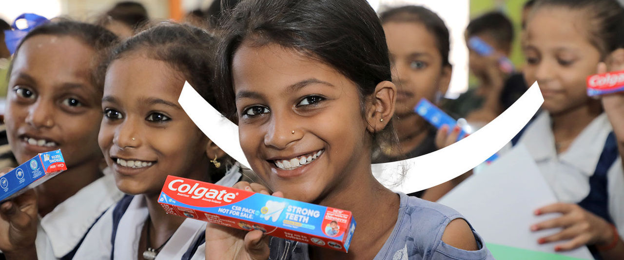 Group of smiling school children holding Colgate toothpaste boxes during an oral hygiene awareness campaign.